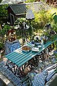 Vintage-style garden furniture, plants on table and standard lamp on summery wooden terrace