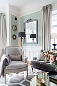 Sessel und Sofa um runden Tisch in lichtdurchflutetem Wohnzimmer mit pastellgrüner Wand