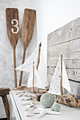 Sailing boat ornaments made from driftwood and fabric remnants next to paddles in corner
