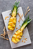 Pineapple boats with roasted coconut chips and wooden skewers on a white marble platter