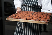 Tray of freshly made chocolate truffles being held by a chef