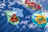 Pretzel on hand-sewn picnic bag and plates of sliced oranges and watermelons