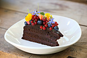 A piece of chocolate cake with berries and edible flowers