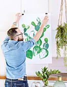 Man hanging up painting of cactus