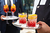 A waiter carrying cocktails on a tray (Campari Soda and Aperol Spritz)