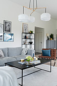Sofa, leather easy chair and designer lamp above coffee table in grey-and-white interior
