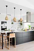 White, open-plan kitchen with three pendant lamps above black kitchen counter
