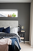 Blanket on double bed with button-tufted headboard against dark grey wall