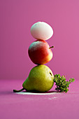 A pear, an apple and an egg stacked on top of each other with a bunch of thyme