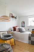 Scatter cushions on single bed in white guest room with wooden floor