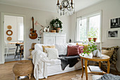 Runder Tisch, Sofa mit weißen Hussen, im Hintergrund Highbord und Gitarre im Wohnzimmer im Landhausstil
