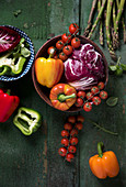 Paprika, Tomaten und Radicchio in Schale auf grünem Holzuntergrund