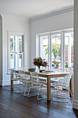 Filigree white chairs on the wooden table in front of the window to the garden