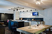 Island counter, rustic wooden table and various spotlights in black-and-white kitchen
