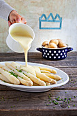 Sauce Hollandaise being poured over white asparagus
