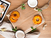 Leaves of fresh mint, slices of sweet pineapple and halves of tasty coconut on lumber tabletop near tablet and napkin