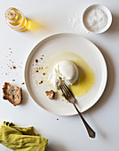 Plate with delicious fresh burrata placed on white tabletop near piece of bread and oil with salt