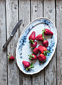 Plate of delicious ripe strawberries placed on wooden tabletop near blue napkin and metal knife