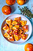 Cut red orange in a plate. Whole red oranges and thyme on a blue table