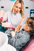 Little girl learning how to brush teeth in dental clinic