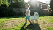 Toddler pulling pram on grass
