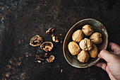 A hand holding a bowl of walnuts