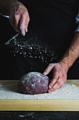 Purple loaf of spelt aronia berry powder bread being dusted with flour