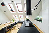 Kochinsel und Esstisch mit schwarzen Stühlen in hohem Raum mit Dachschräge