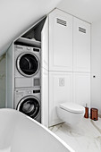 Washing machine and tumble dryer in fitted cupboard in elegant bathroom