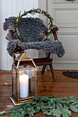 Candle lantern on floor, fir branches, and chair with sheepskin blanket and wreath on veranda