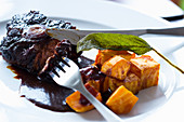 Oxtails in red wine gravy with fried sweet potatoes and a sage leaf
