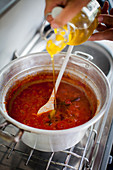 Tomato sugo being seasoned with olive oil