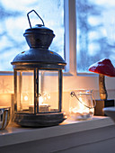 Tealights burning in lantern and candle lantern on windowsill