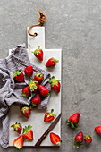 Fresh strawberries in striped kitchen towel on white marble board over grey concrete background