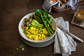 Vegan breakfast bowl with scrambled tofu, green asparagus, sesame-coated mushrooms, avocado and spinach