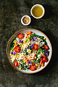 Couscous with parboiled vegetables baby carrots, green beans, sweet corn, spinach served in ceramic plate with tomatoes, sesame and edible flowers