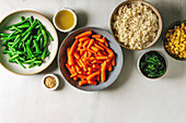 Couscous with parboiled vegetables baby carrots, green beans, sweet corn, spinach in separate ceramic plates with sesame seeds and olive oil