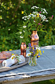 Wild summer flowers in copper-coloured containers on table outside