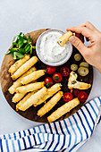 Woman eating stuffed phyllo rolls dipping into a yogurt sauce, tomatoes, mint and pickles accompany