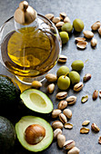 Healthy fats - a jar of olive oil, with olives, pistachio nuts and avocados sitting beside