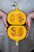 Person holding pumpkin with orange flesh cut in half