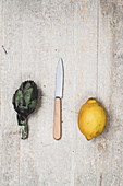 Fresh lemon, artichoke and kitchen knife on grey background