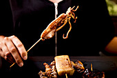 Female eating appetizing grilled hot squid skewer over plate with meat and vegetable skewers on wooden table in cafe