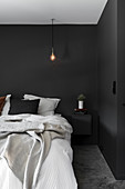 Schlafzimmer mit schwarzen Wänden und Glühbirne als Hängeleuchte