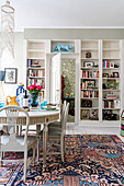 Stylish white dining table and fitted bookcase in bright interior