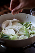 A hand spicing onions in a pan