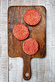 Raw hamburger patties on a wooden cutting board
