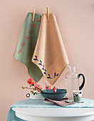 Printed tea towels hung from line against pink wall