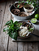 From above of arranged bowls with dry spices and served Pho soup with noodles on marble board