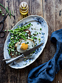 From above of served plate with bread toast with sauteed green peas and fried egg on wooden table